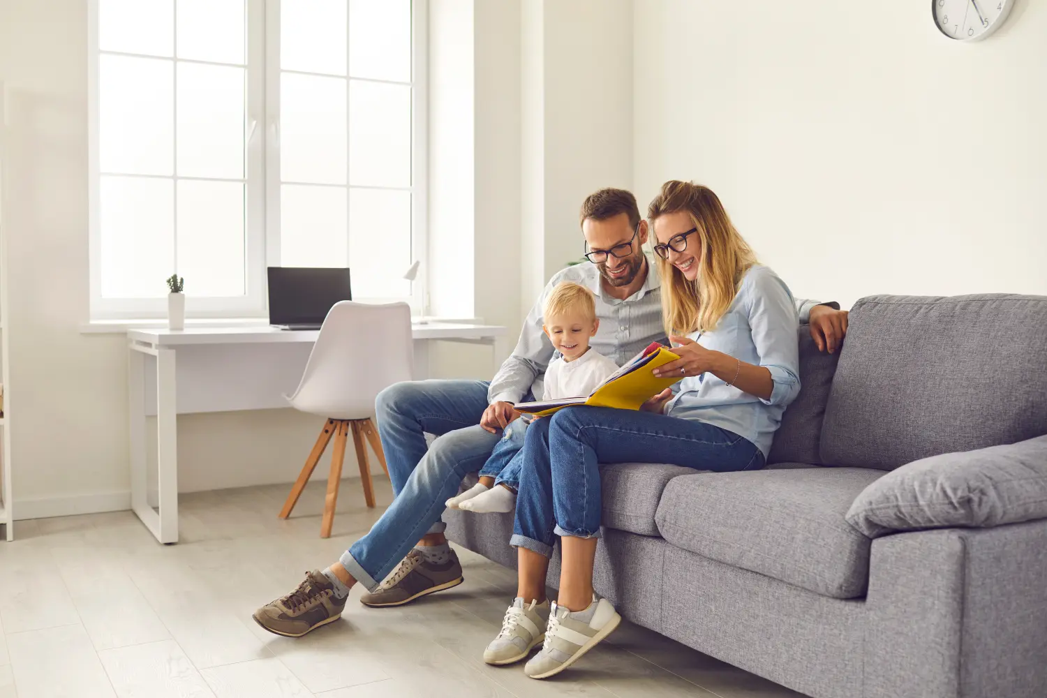 Glückliche Eltern und Kind sitzen auf dem Sofa, lesen ein Buch mit Geschichten oder blättern im Familienalbum